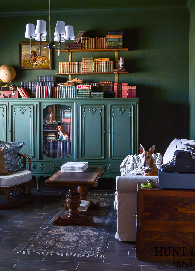 Try your hand at stylish storage with opening shelving and furniture made to look like a built in. This stunning moody green library room will answer the question , why open shelving over built-ins cabinets! #weekendproject #openshelving #goldaccents #libraryroomidea #studydecorideas #builtinbookcase #englishcountry