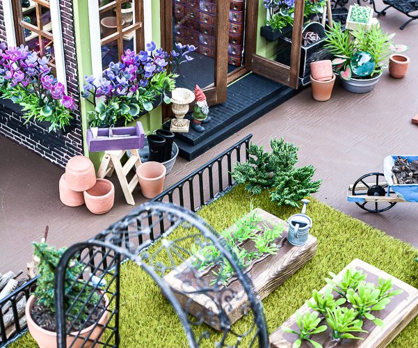 Tour a miniature vintage garden shop dollhouse for great ideas for your own dollhouse decor. See how to make a cozy home, lush garden and outdoor miniature yard! COmplete with garden gnomes, miniature potted plants and sitting areas. #dollhouse #miniatures #DIYdollhouse #vintagegarden #tinydecor