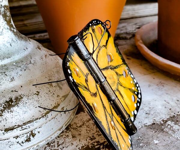 Wonder what to do with old door hinges? Try this upcycled door hinge butterfly project for a fun and beautiful addition to your spring decor ideas. These painted butterflies are perfect for your patio and potted plants. Truly adorable yard art you can DIY with thrifted or left over materials! #butterflyart #doorhinge #upcycledcraft #springdecor #springcraft